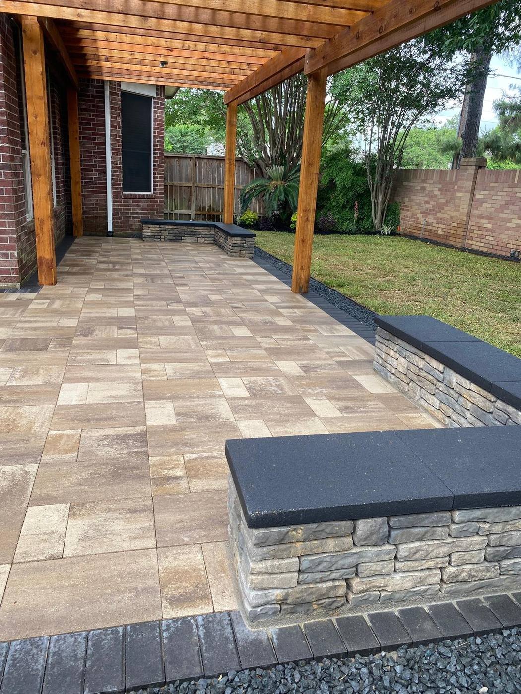 Paver patio under a cedar pergola with built-in stone seating walls