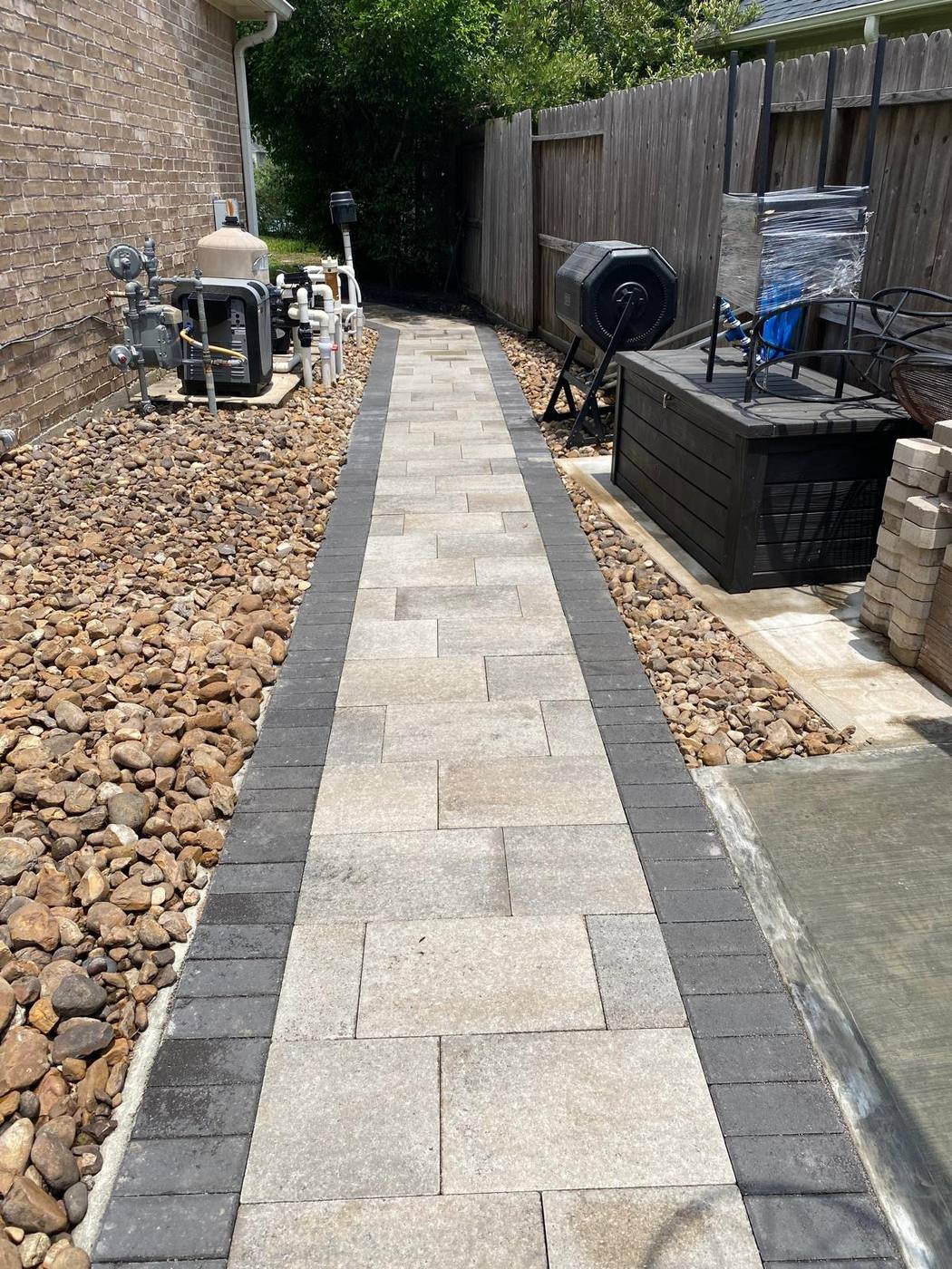 Paver side-yard walkway with a dark border and river rock beds