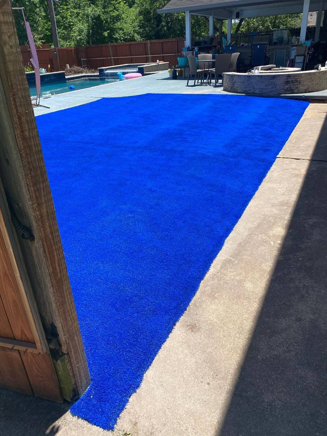 Custom blue synthetic turf area beside a backyard pool and outdoor kitchen
