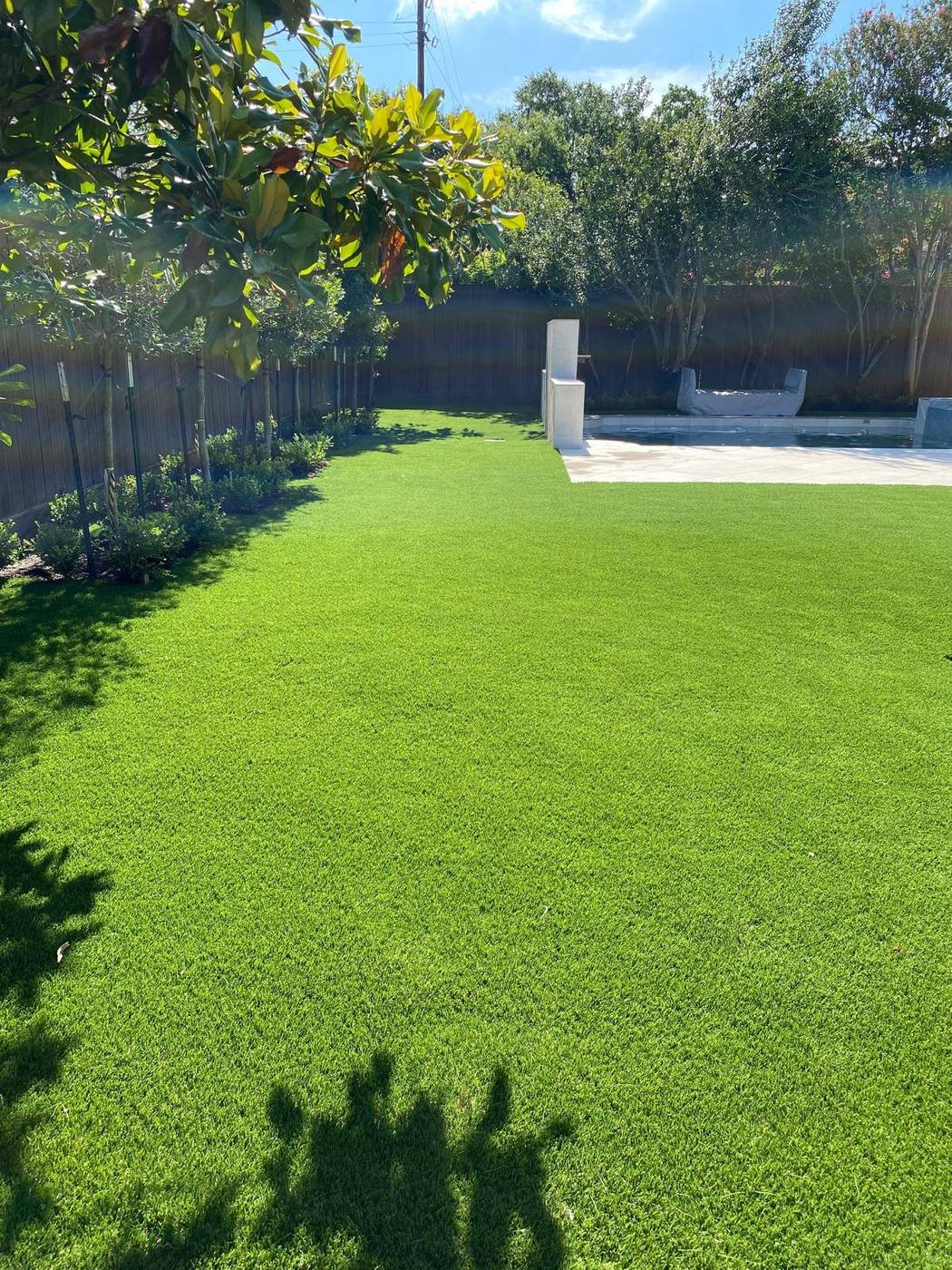 Large synthetic turf backyard bordered by planting beds, next to a pool